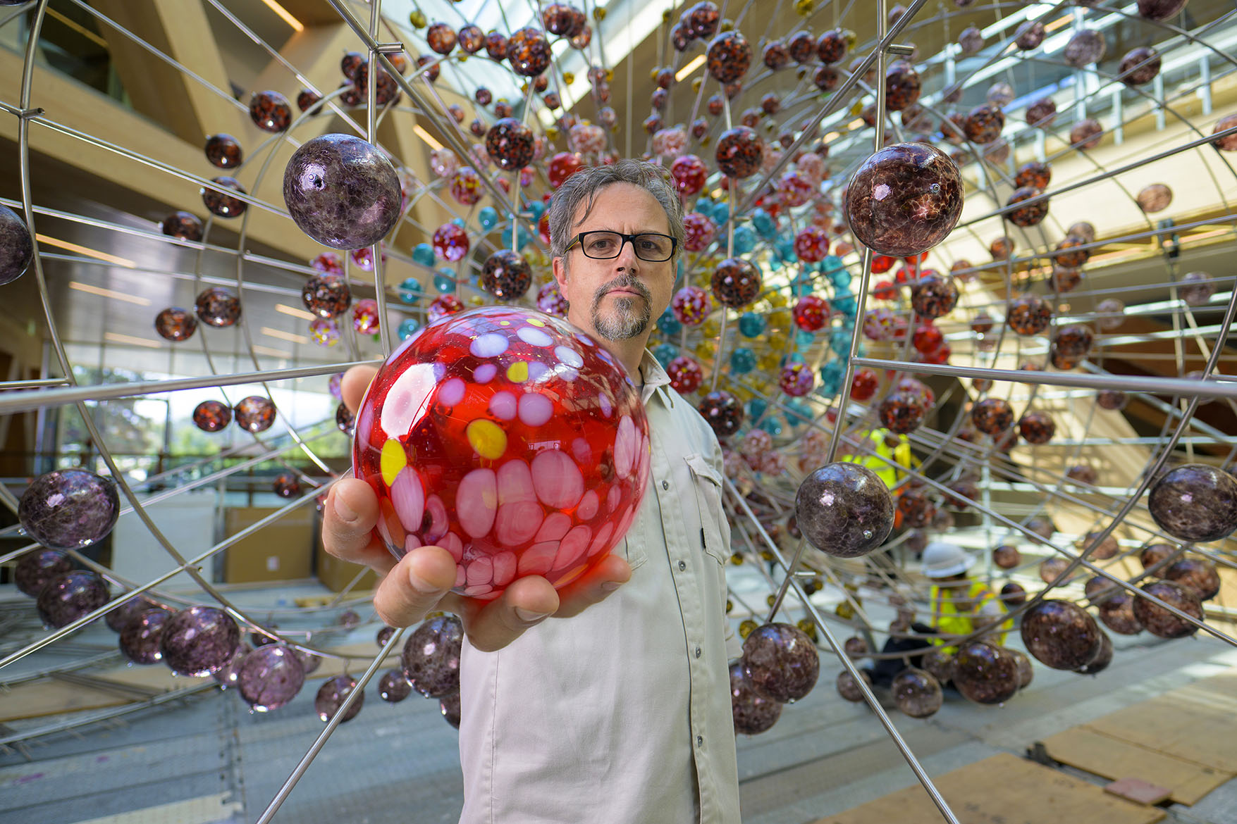 Damián Ortega, holding a red glass sphere, standing in front of the Magnetic Field installation.