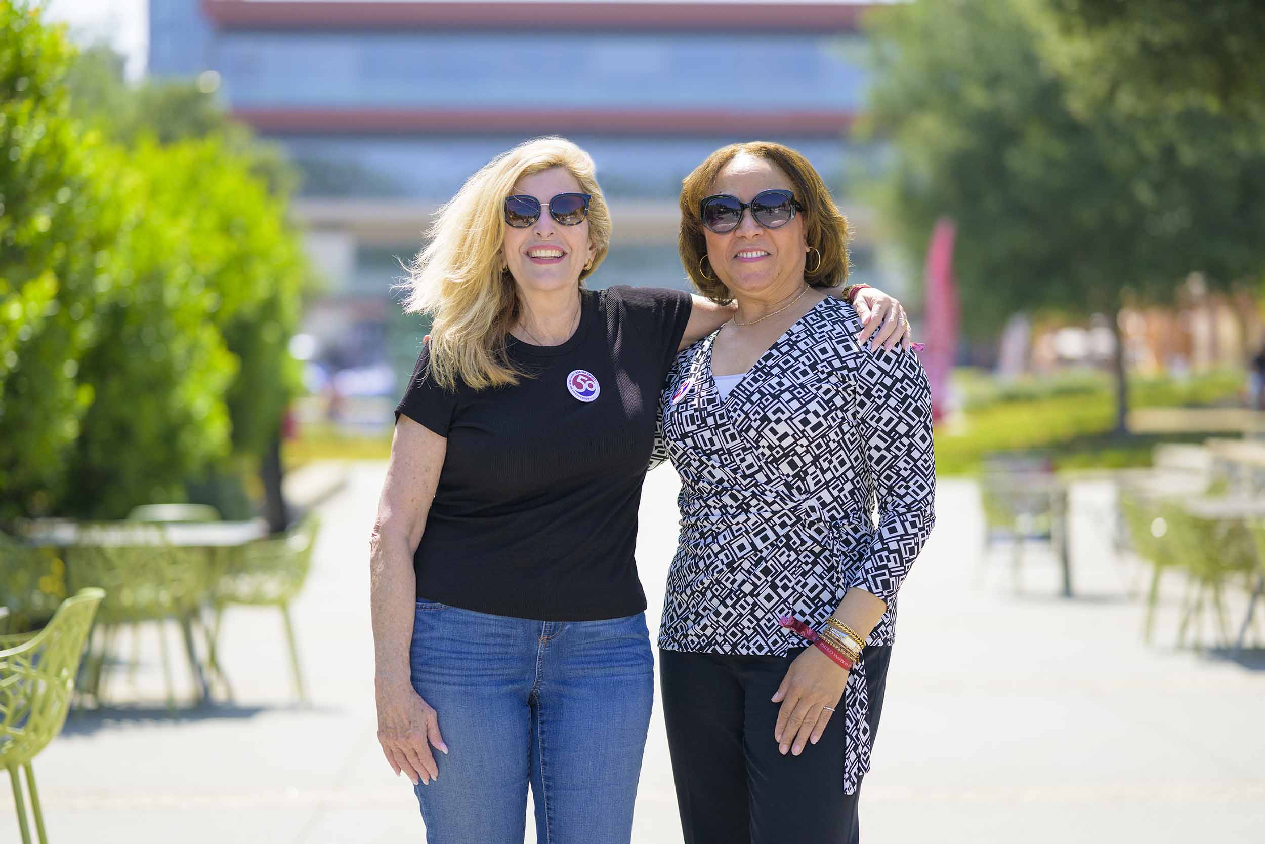 Mari Adam ’80 (left) and Lorraine Bains ’88 standing together on the North Mall.