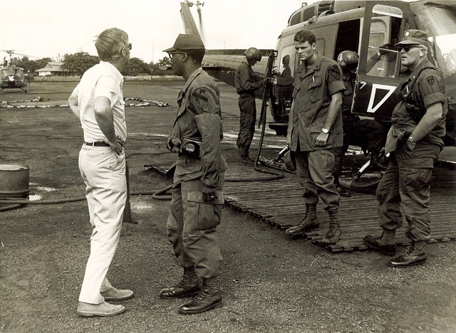 Men on military base in uniform in front of helicopter talking.