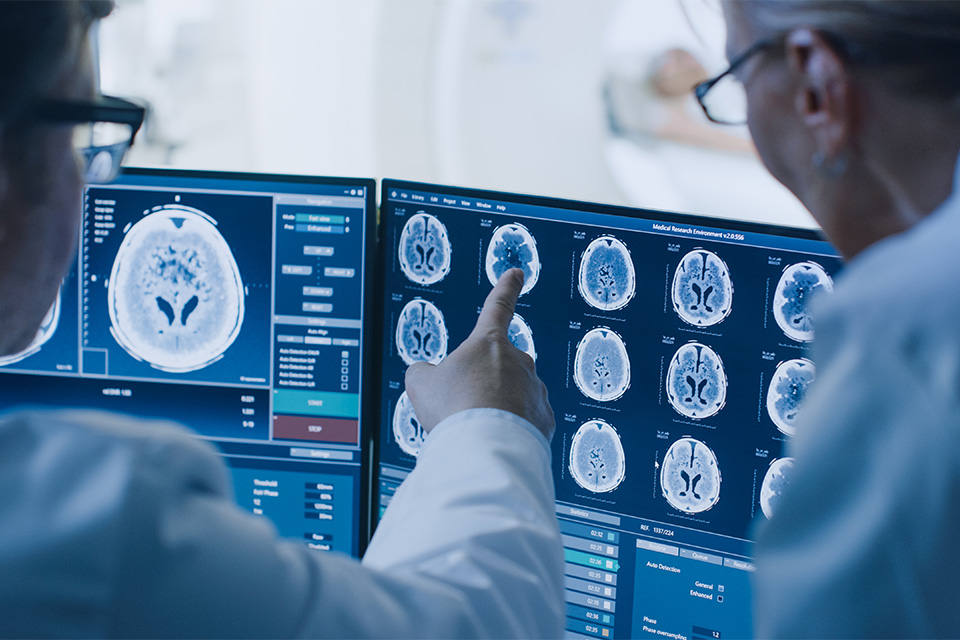 Stock image of researchers in lab coats and goggles examining brain scans on a computer screen.