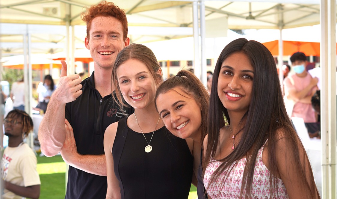 Four students smile together for the camera at the SIF booth during the Club and Institute Fair