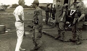 Men on military base in uniform in front of helicopter talking.