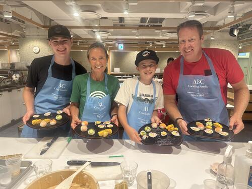 Family with two boys, mom, and dad, in a cooking class wearing aprons and making food.