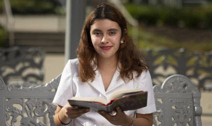 Marycarmen Montarez ’22 holds open a book while sitting on a bench from Artist Chris Burden’s Meet in the Middle public art sculpture.